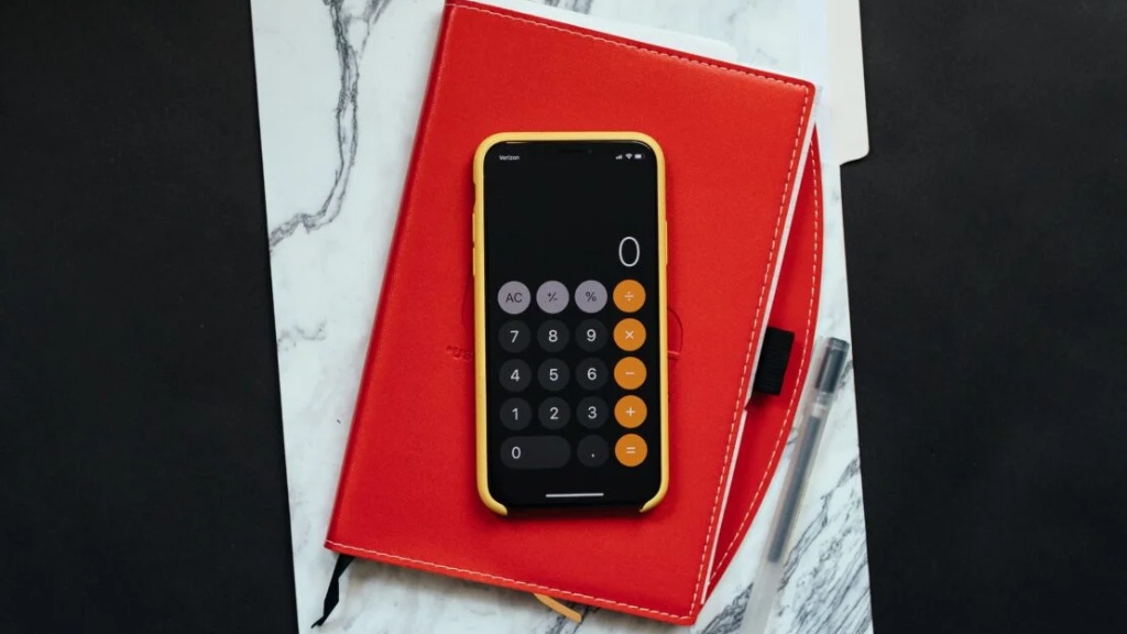 Aplikacja kalkulatora włączona na telefonie w żółtym pokrowcu leżącym na czerwonym notesie